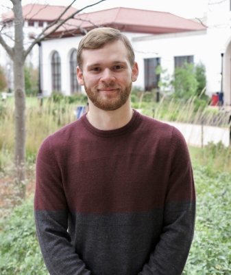 A picture of Justin Savage, a white man, average height, dirty blond hair, wearing a red and black sweater