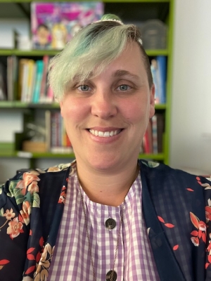 Caucasian women blue hair with bangs posing in front of shelf of books