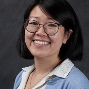 Headshot of bespectacled woman with short black hair, a white blouse and periwinkle cardigan.