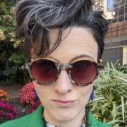 picture of Kathleen DiGiulio, a white woman with dark hair, wearing sunglasses and a green coat