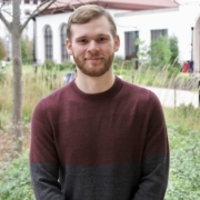 A picture of Justin Savage, a white man, average height, dirty blond hair, wearing a red and black sweater