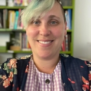 Caucasian women blue hair with bangs posing in front of shelf of books